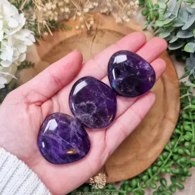 Three Amethyst pocket stones laying on hand