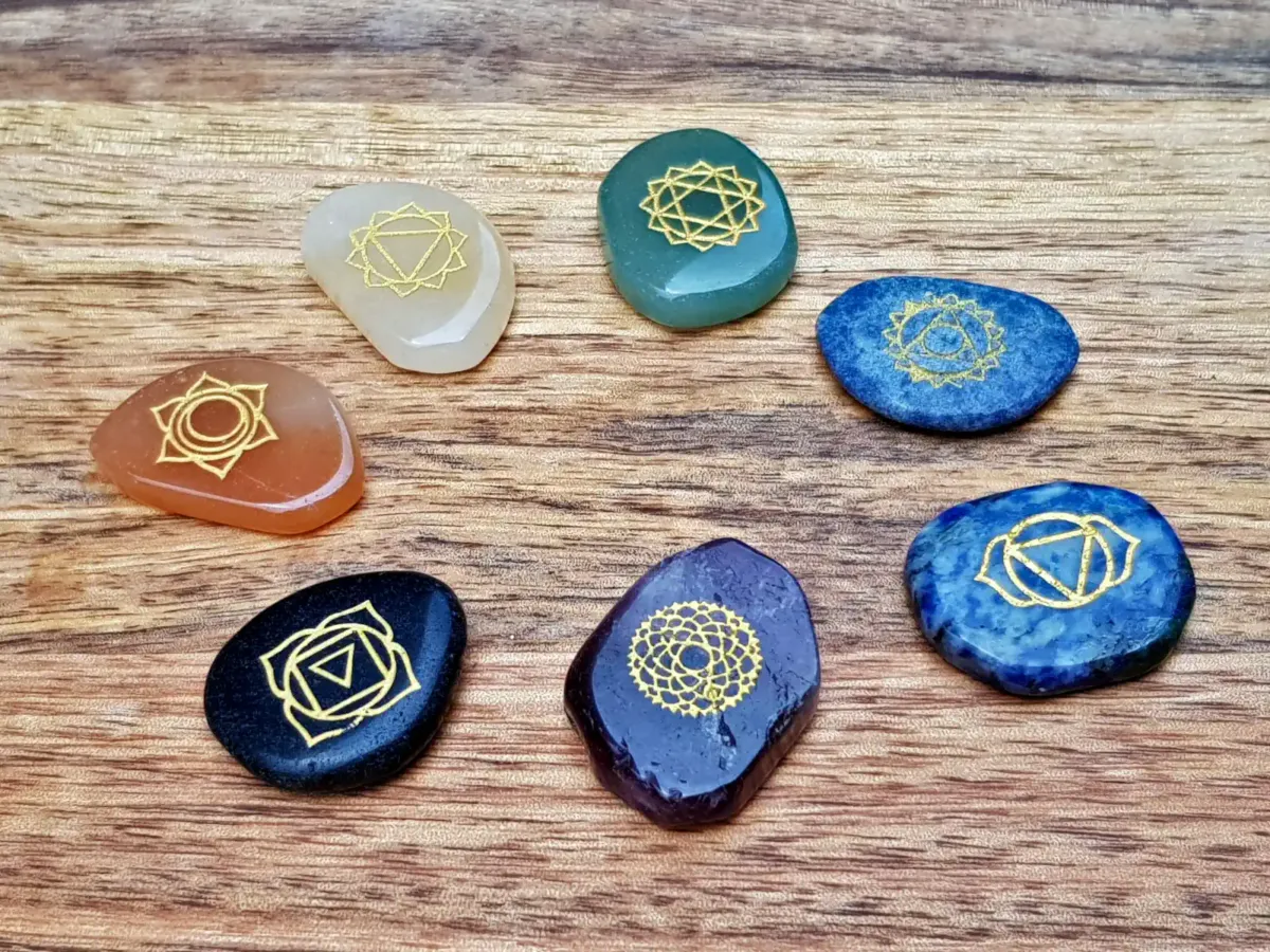 Seven tumbled chakra stones with chakra symbols on a wooden table