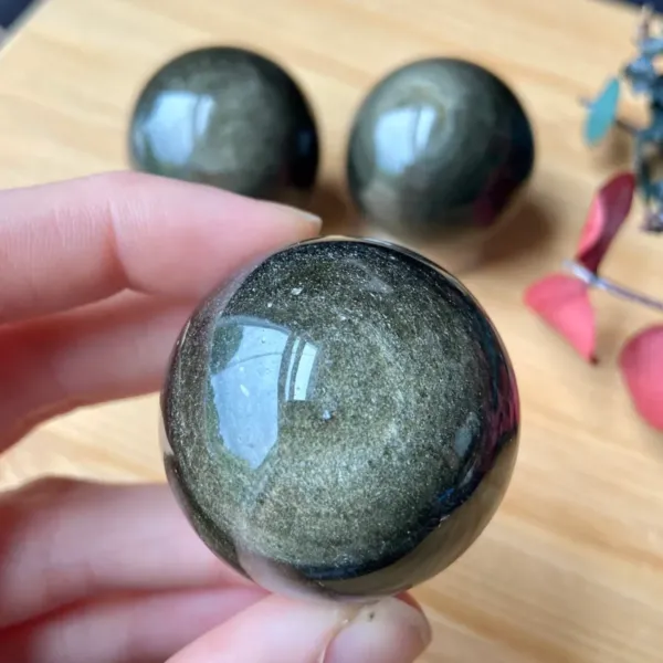 Golden Sheen Obsidian Spheres - one being held and two in the background