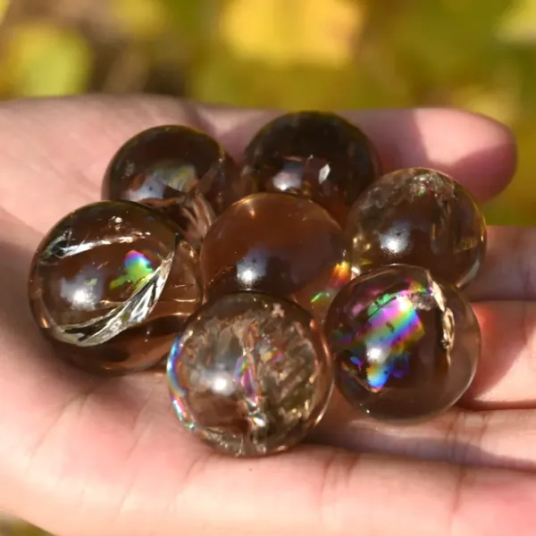 Seven pieces of Smokey Quartz Rainbow Spheres on palm of the hand.